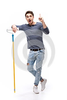 Handsome man holding paint roller and pointing up isolated on white