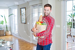 Handsome man holding paper bag full of fresh groceries at home