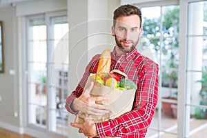 Handsome man holding paper bag full of fresh groceries at home