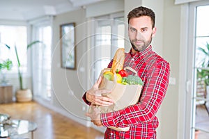 Handsome man holding paper bag full of fresh groceries at home