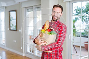 Handsome man holding paper bag full of fresh groceries at home