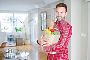 Handsome man holding paper bag full of fresh groceries at home