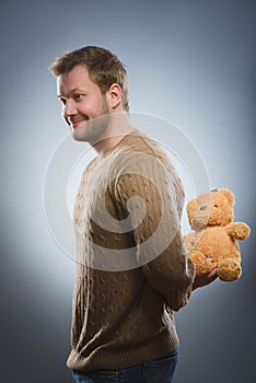 Handsome man is holding a teddy bear and smiling on gray background