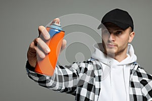 Handsome man holding used can of spray paint on grey background