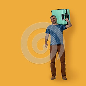 Handsome man holds plastic suitcase on his shoulder. Front view of middle-aged caucasian man holding green suitcase