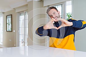 Handsome man at home smiling in love showing heart symbol and shape with hands