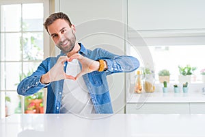 Handsome man at home smiling in love showing heart symbol and shape with hands