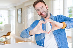 Handsome man at home smiling in love showing heart symbol and shape with hands