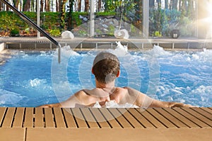 Handsome man in hot tub spa in luxurious hotel with big glass wi