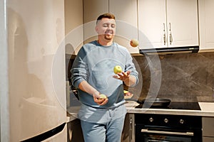 Handsome man juggle with apples in modern kitchen