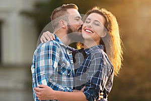 Handsome man kissing tenderly his girlfriend in cheek outdoors