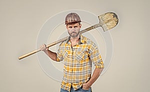 handsome man laborer in construction safety helmet and checkered shirt on building site with shovel, industry