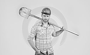 handsome man laborer in construction safety helmet and checkered shirt on building site with shovel, industry