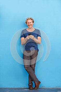 Handsome man leaning against blue wall and using cell phone
