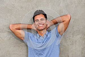 Handsome man leaning against wall with hands behind head