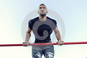 Handsome man lifting his torso above the bar while he works out outside, street workout and healthy lifestyle