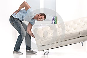 Handsome man lifting sofa and feeling pain.