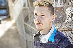 Handsome man listen to music with headphones near the fence outdoors.