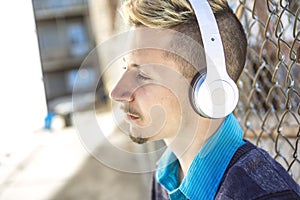 Handsome man listen to music with headphones near the fence outdoors.