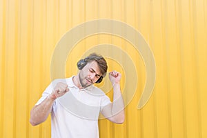 Handsome man listens to music in wireless headphones and dances against the backdrop of a yellow wall. Musical concept
