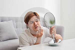 Handsome man looking at himself in mirror. Squeezing pimple.
