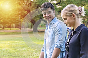 Handsome man looking at his girlfriend while walking on the green meadow in public park. Cheerful couple walk relaxation