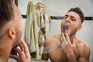 Handsome man looking in mirror at his teeth