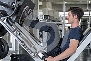 Handsome man lowering weight training legs on leg press machine and working out in the fitness gym