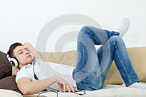 Handsome man lying on couch with headset listening to music