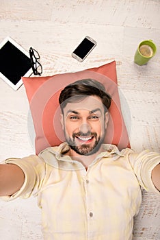 Handsome man lying on the floor on pillow and making selfie