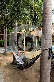 Handsome man lying on hammok and using smartphone outdoors