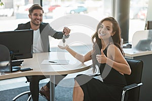 Handsome man manager giving car keys after holding successful deal to his beautiful woman client at dealership office