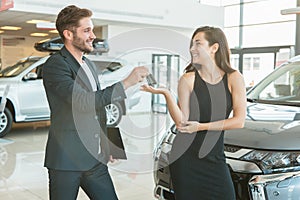 Handsome man manager giving car keys to beautiful woman client standing near brand new car after succesful deal in
