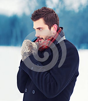 Handsome man in mittens freezes outdoors in winter