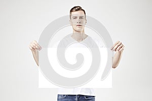 Handsome man model standing with blank big poster or sheet in hands, isolated on white background, wearing jeans and t-shirt.