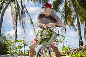 Handsome man with moustache on the bicycle with basket made of palm leaves wearing sunglasses and transparent t-shirt