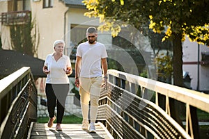 A handsome man and an older woman share a serene walk in nature, crossing a beautiful bridge against the backdrop of a