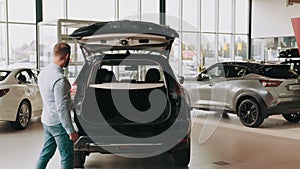 Handsome man opening empty car trunk of expensive black automobile. Young customer checking car trunk lock of the car he