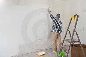 Handsome man painting wall with roller brush. Renovation house