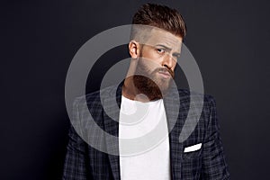 Handsome man with perfect hairdo and beard looking wonderingly at camera while standing against black background