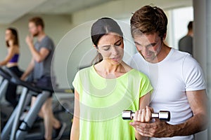 Handsome man personal trainer helping fit woman working with dumbbells in fitness gym club