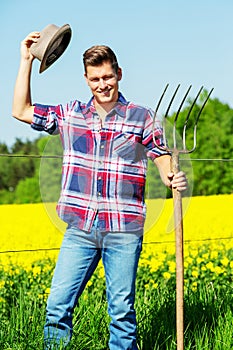 Handsome man with pitchfork standing in front of yellow field