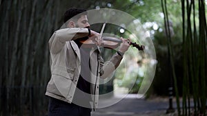 handsome man is playing violin in garden in summer, romantic musician play fiddle outdoor