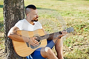 Handsome man plying guitar in a summer park photo
