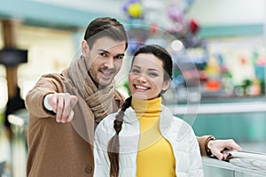 Handsome man pointing with finger at camera ad smiling girl in