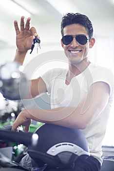 Handsome man, portrait and motorcycle keys with helmet and sunglasses for transportation vehicle in garage. Young male