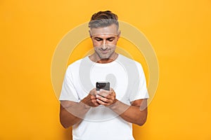 Handsome man posing isolated over yellow wall background using mobile phone
