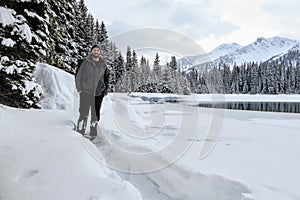 A handsome man posing for a photo dressed in a winter coat and toque, with a forest and lake in background