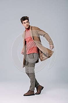 handsome man posing in stylish beige coat on grey.