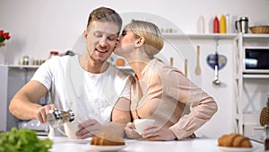 Handsome man pouring brewed coffee to girlfriend, getting kiss from beloved